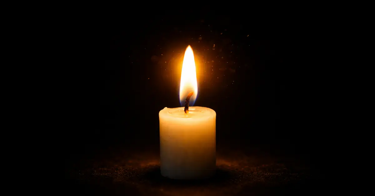 Vela encendida en la oscuridad con una luz pequeña pero firme, símbolo de la vida joven que iluminó antes de partir
